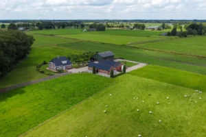 Luchtfoto van een boerderij, omgeven door een groene weide met grazende schapen.