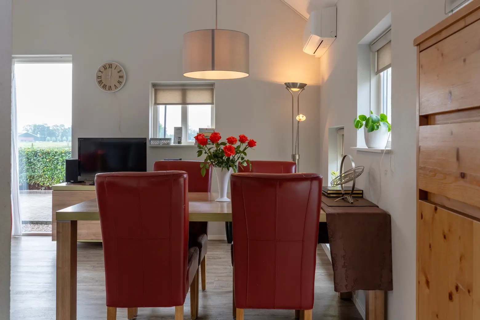 Eetkamer met rode rozen op een bruine tafel.