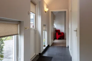 Een hal die uit kijkt op de hoofdslaapkamer met een rode stoel in de zithoek